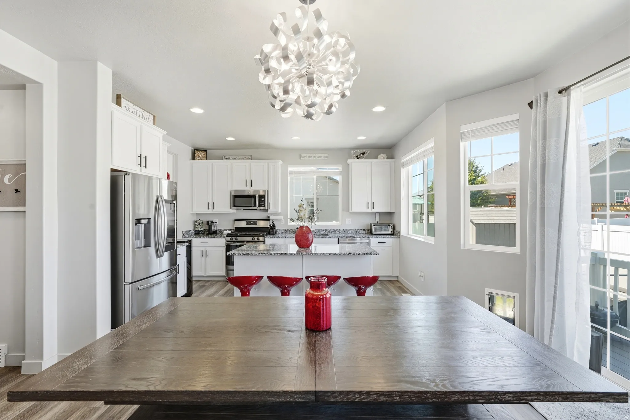 Kitchen featuring white cabinetry, stainless steel appliances, a center island with granite-style countertops, wood-finish flooring, and a modern chandelier