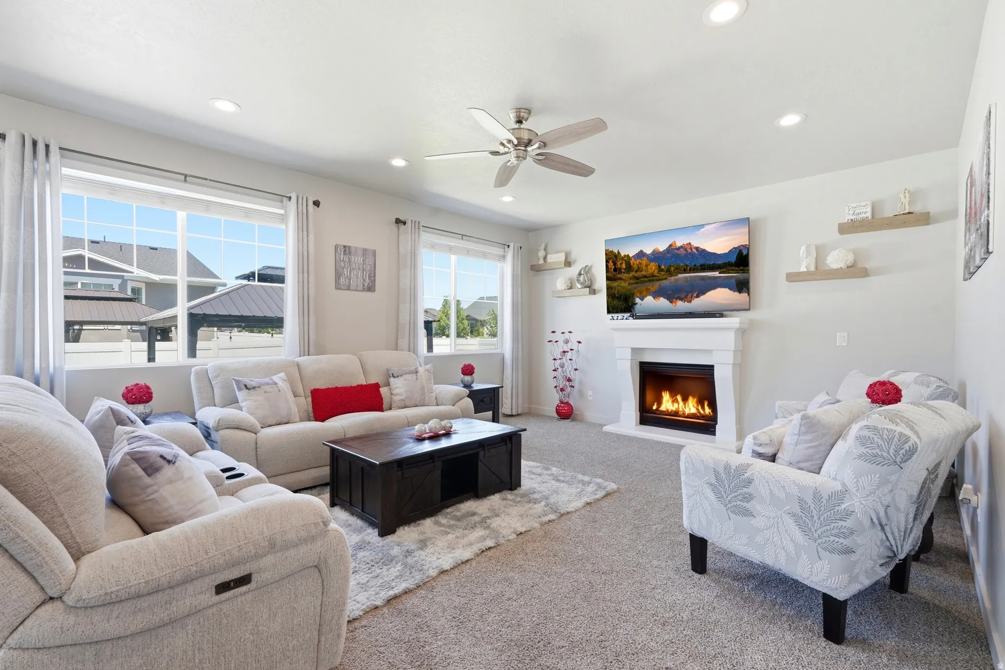 Spacious living area featuring a fireplace with a white mantel, recessed lighting, a ceiling fan, and multiple windows
