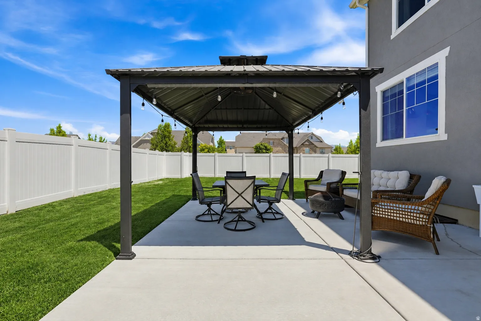 Expansive concrete patio featuring a gazebo, a manicured lawn, and a white privacy fence