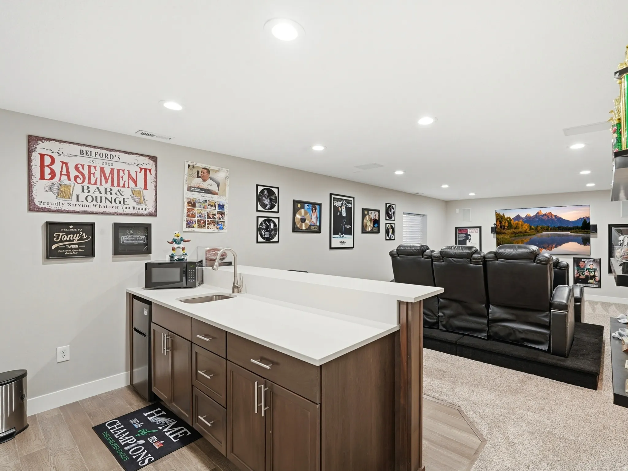 Finished basement with a wet bar featuring wood-finish cabinetry, quartz countertop, and a stainless steel sink