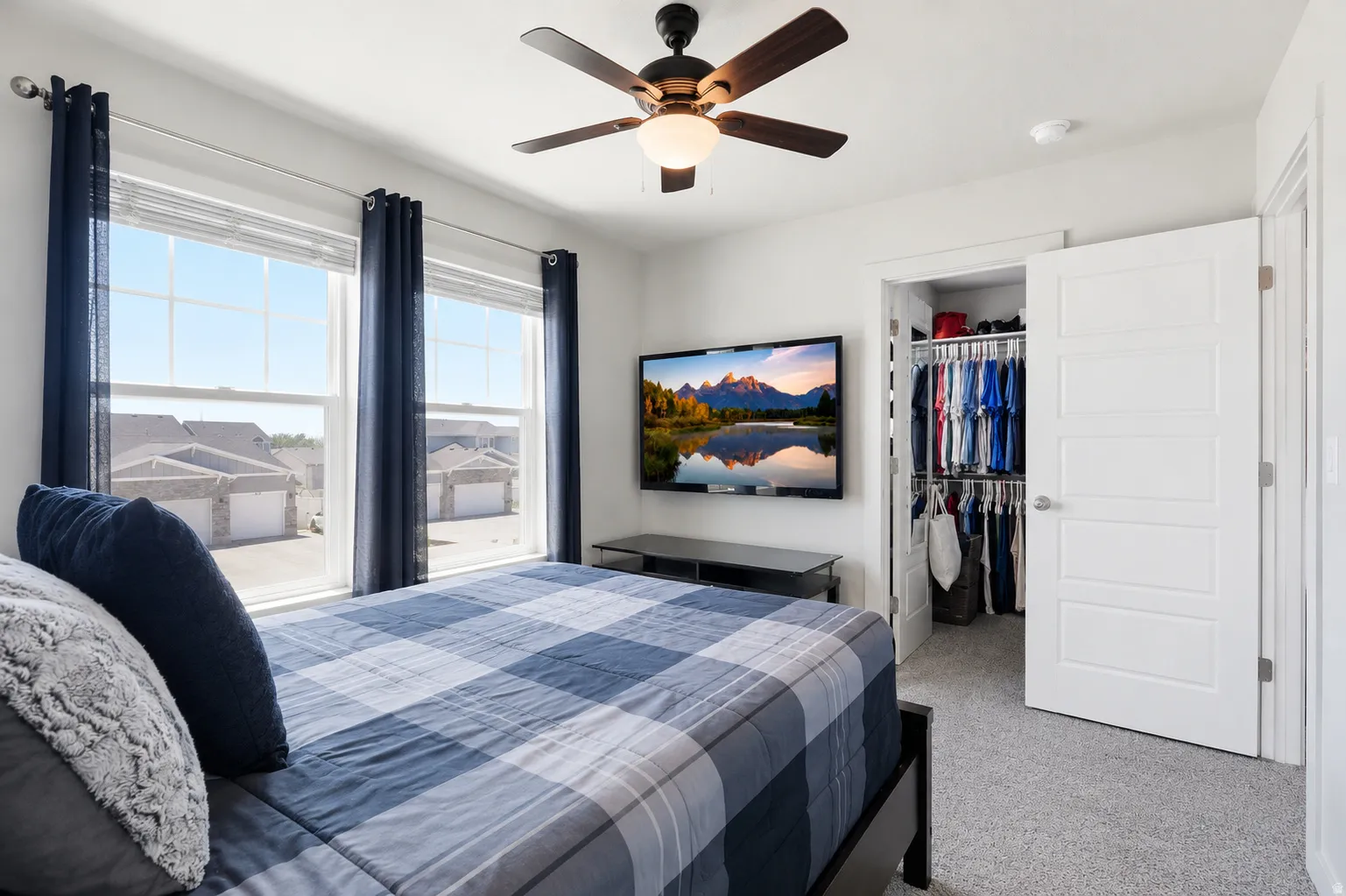 Carpeted bedroom featuring two large windows, a ceiling fan with integrated lighting, and a walk-in closet with built-in shelving and hanging rods