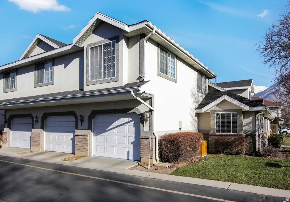 Multi-level exterior featuring light-colored siding, multiple garage doors, and dark shingle roofing