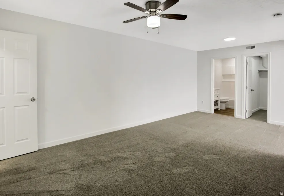 Spacious room featuring neutral carpeting, a ceiling fan with integrated lighting, and white trim