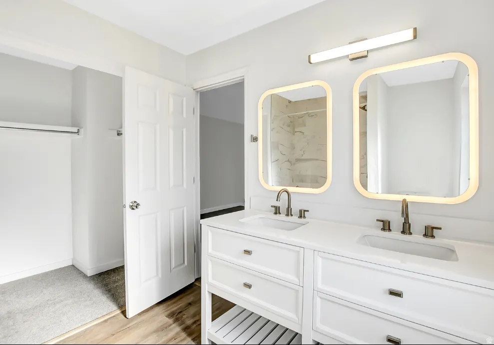 Dual vanity with white cabinetry and integrated sinks, illuminated by backlit mirrors and an overhead light bar