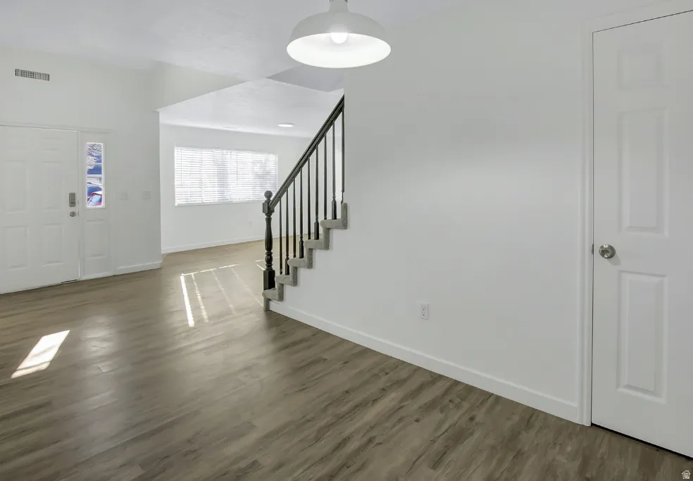 Entry foyer featuring a white paneled door with decorative glass inserts, wood-finish flooring, a contemporary pendant light fixture, and a staircase with a dark wood-finish handrail and black balusters