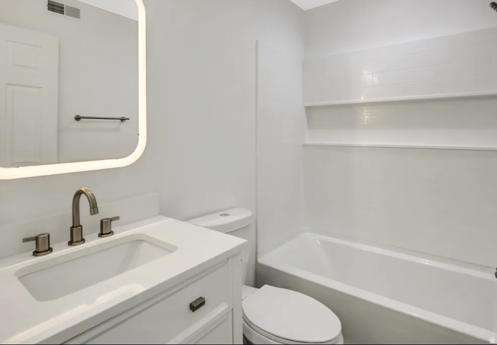 Bathroom featuring a white vanity with an integrated sink, brushed bronze faucet, and an illuminated mirror