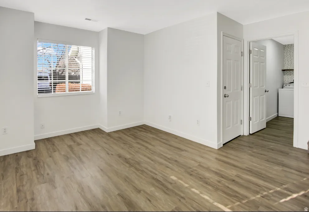 Spacious room featuring wood-finish flooring, white baseboards, and a window with horizontal blinds