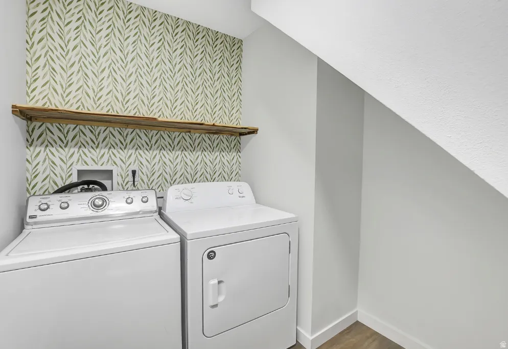 Laundry area featuring patterned wallpaper, a rustic wood shelf, and wood-finish flooring