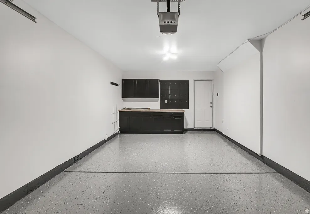 Garage space featuring an epoxy-coated floor, built-in dark cabinetry with a wood-finish countertop, and a white entry door