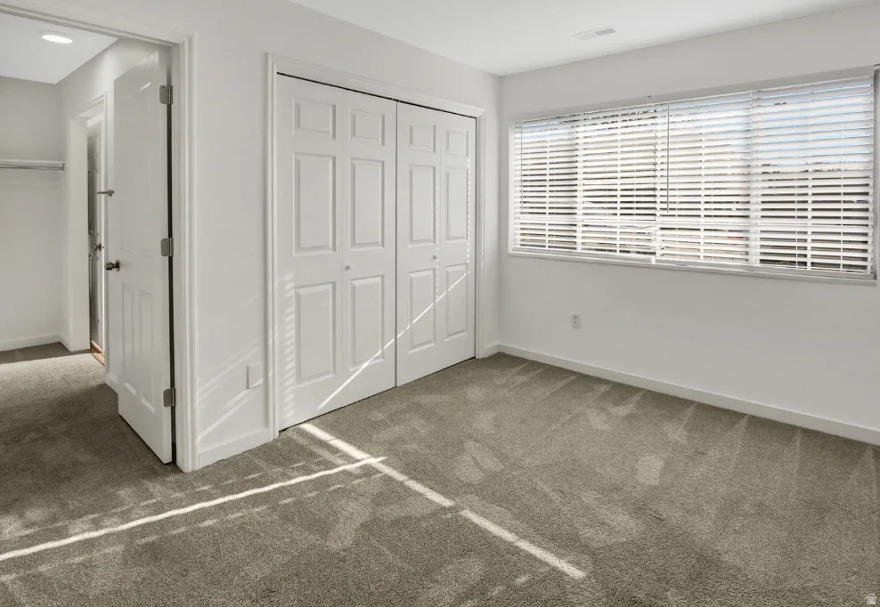 Carpeted room featuring a double bi-fold closet, white interior doors, and a window with horizontal blinds