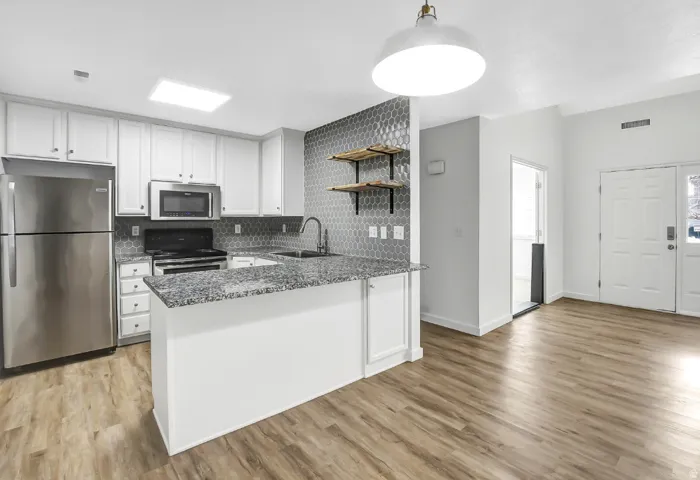 Open-concept kitchen with white cabinetry, stainless steel appliances, granite-style countertops, and hexagon tile backsplash