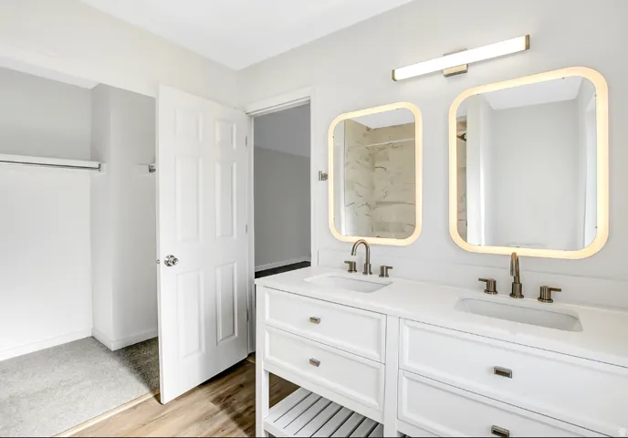 Dual vanity with white cabinetry and integrated sinks, illuminated by backlit mirrors and an overhead light bar