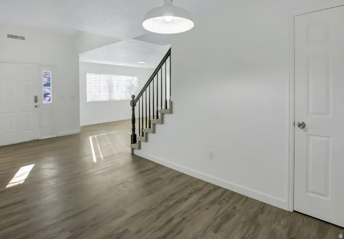 Entry foyer featuring a white paneled door with decorative glass inserts, wood-finish flooring, a contemporary pendant light fixture, and a staircase with a dark wood-finish handrail and black balusters