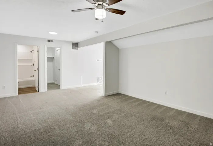 Spacious room featuring neutral carpet flooring, white walls, a ceiling fan with integrated lighting, and white baseboards
