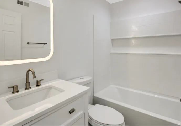 Bathroom featuring a white vanity with an integrated sink, brushed bronze faucet, and an illuminated mirror