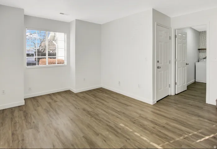 Spacious room featuring wood-finish flooring, white baseboards, and a window with horizontal blinds