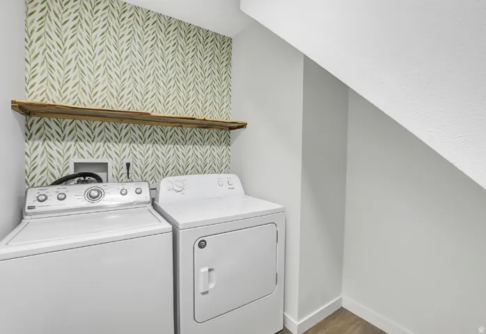 Laundry area featuring patterned wallpaper, a rustic wood shelf, and wood-finish flooring