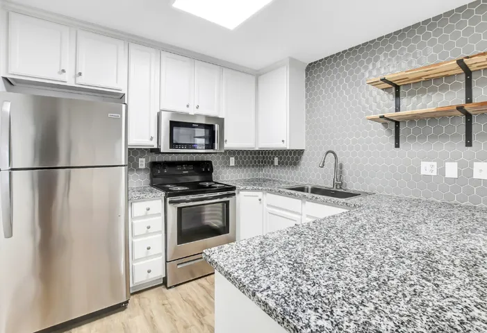Kitchen featuring white cabinetry, stainless steel appliances, granite-style countertops, gray hexagonal tile backsplash, and light wood-finish flooring