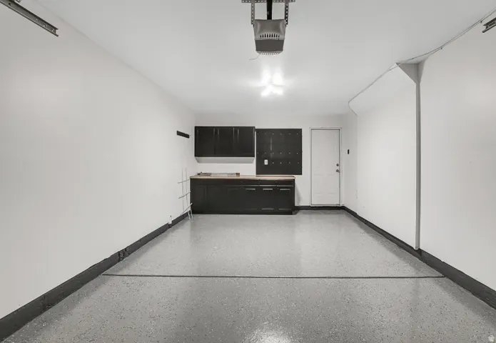 Garage space featuring an epoxy-coated floor, built-in dark cabinetry with a wood-finish countertop, and a white entry door