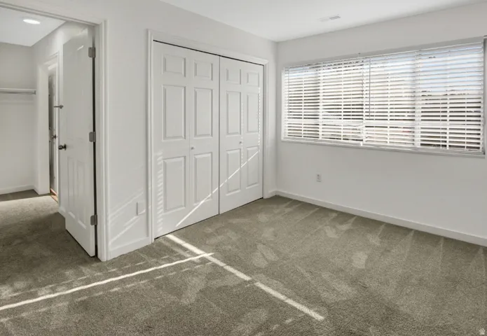 Carpeted room featuring a double bi-fold closet, white interior doors, and a window with horizontal blinds