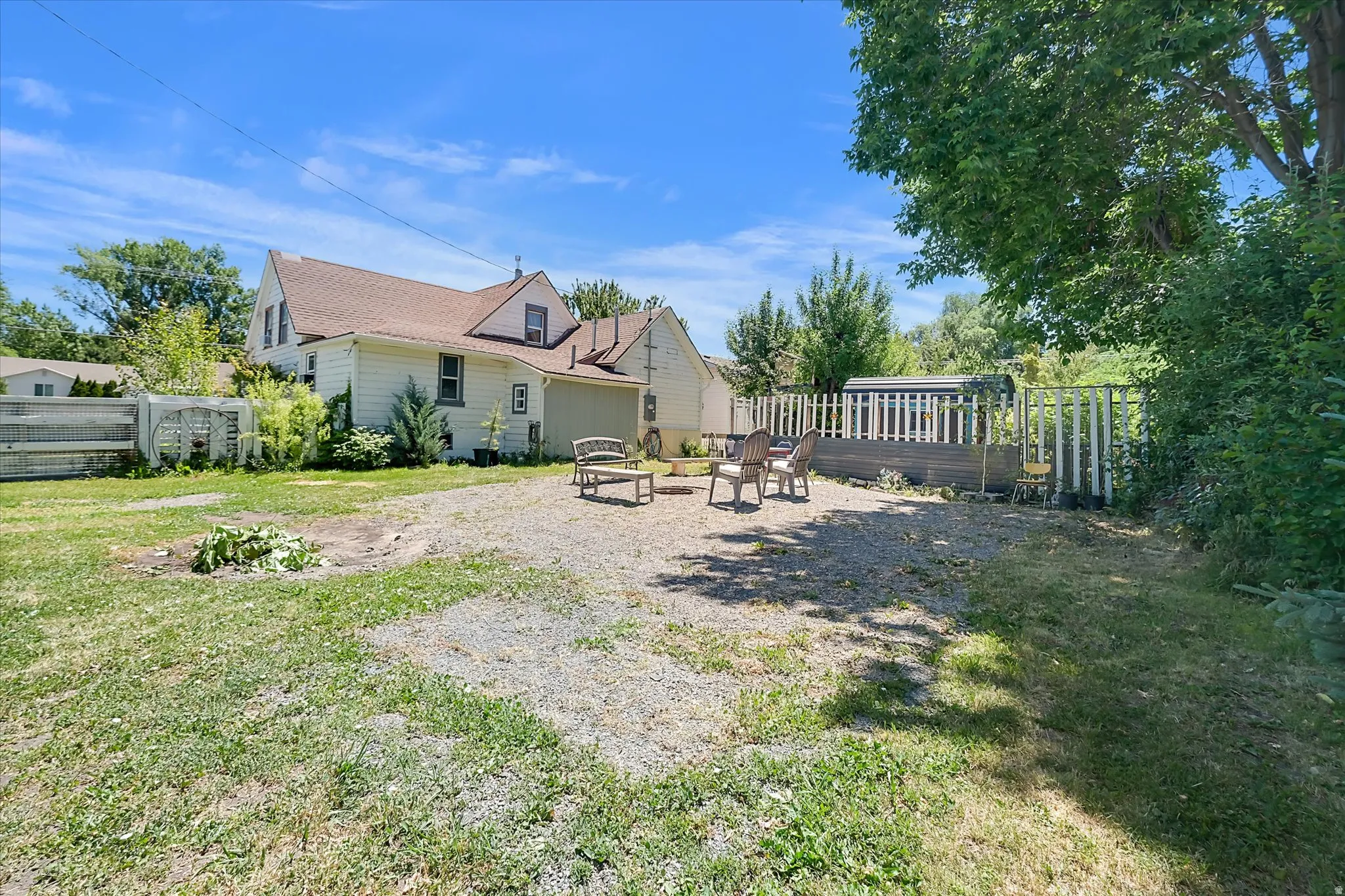 Expansive backyard featuring a gravel patio area, a partial privacy fence, and mature trees