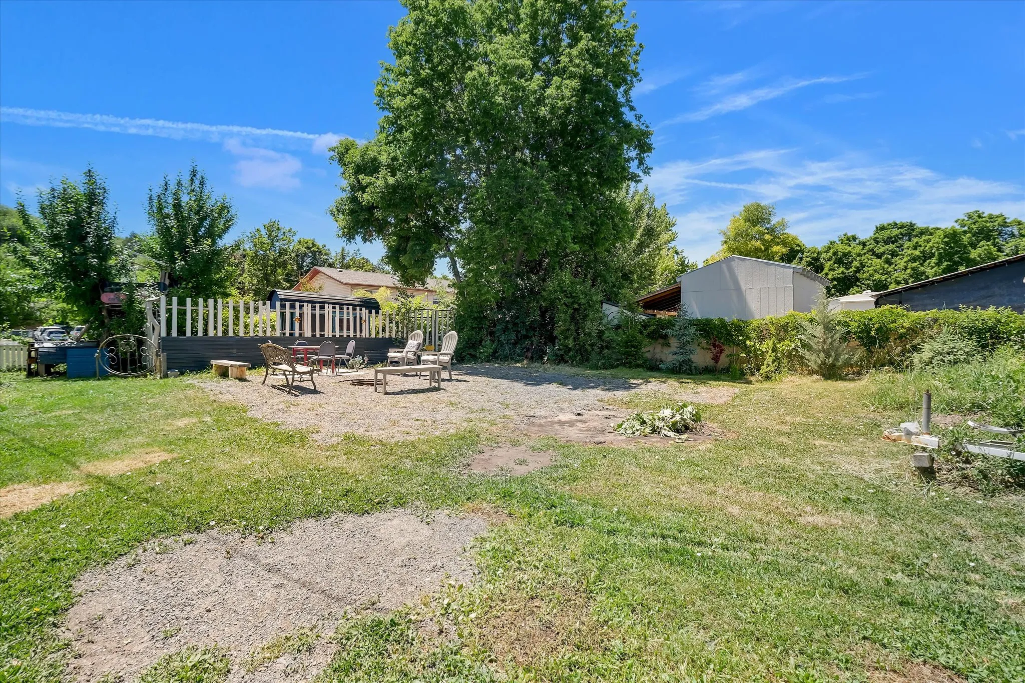 Expansive backyard featuring a gravel patio area, mature trees, and a partial white picket fence