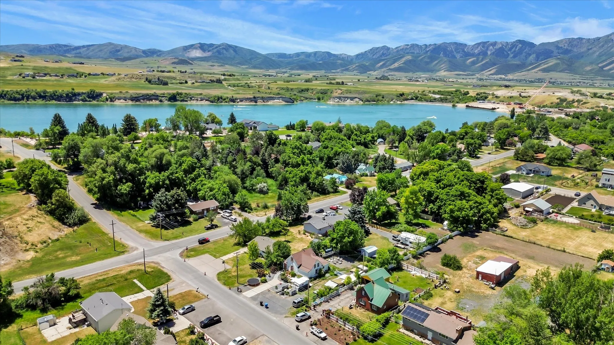 Expansive aerial perspective showcasing a residential area with a prominent body of water, surrounded by green landscapes and distant mountains