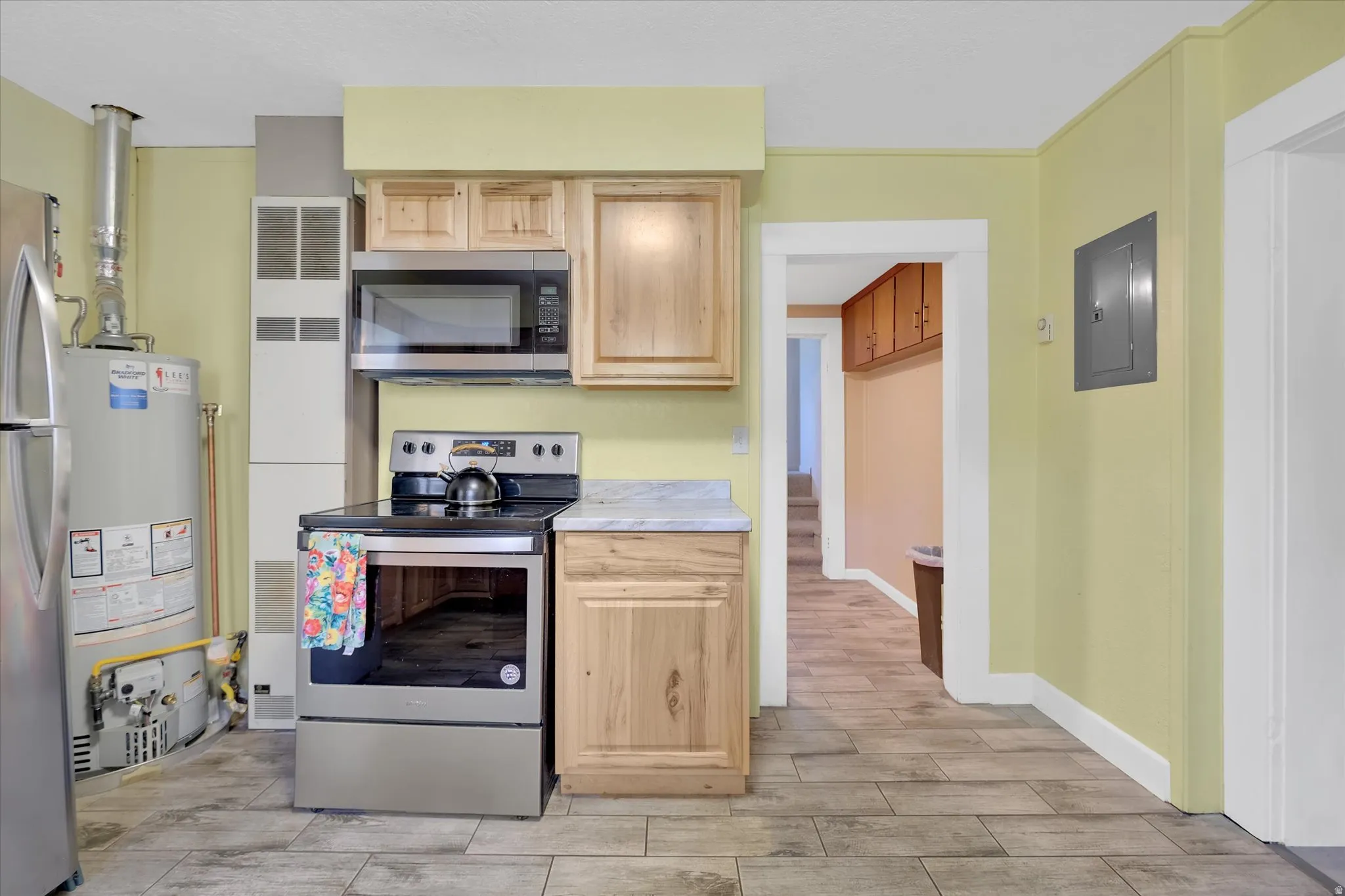 Kitchen area featuring wood-finish flooring, light wood cabinetry, a stainless steel range, and a stainless steel microwave
