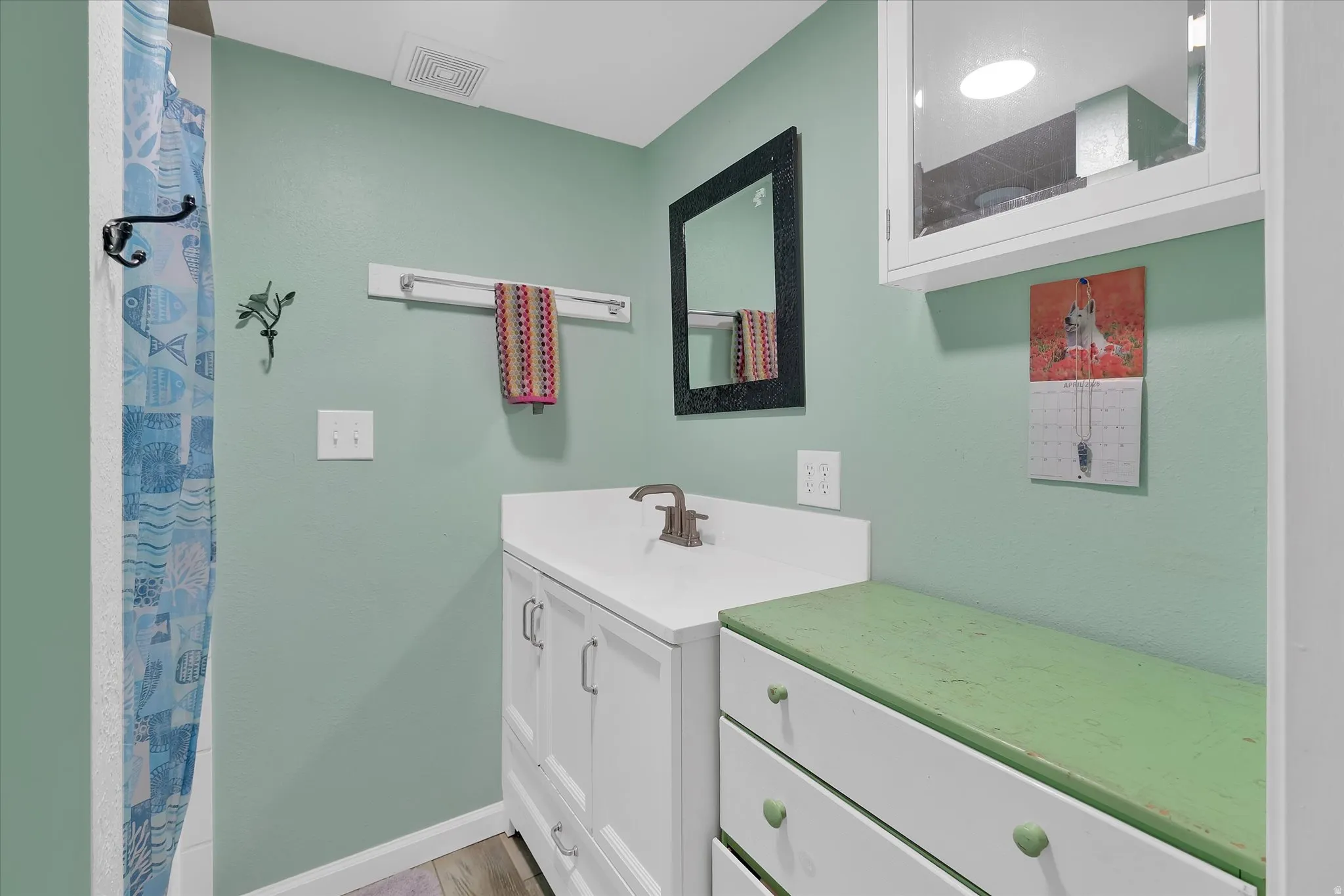 Bathroom featuring a white vanity with integrated sink, brushed nickel faucet, a framed mirror, and wood-finish flooring
