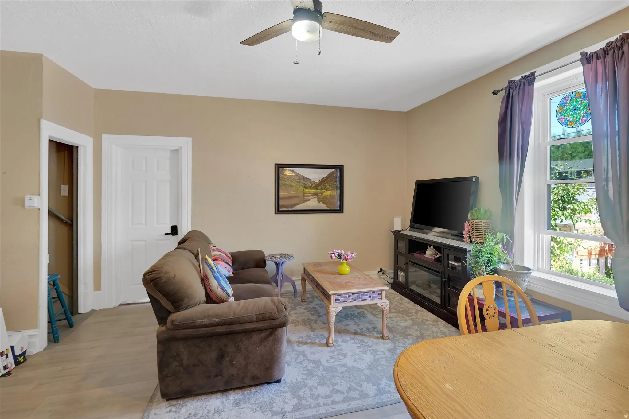 Living area featuring wood-finish flooring, a ceiling fan with integrated lighting, and a multi-pane window