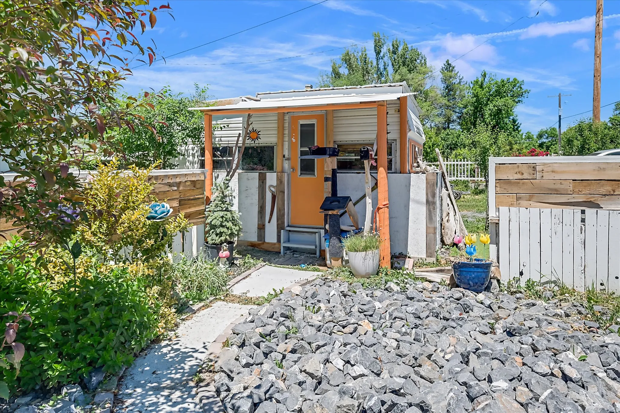 Small dwelling with an orange door, a covered porch supported by wood posts, and a white metal roof