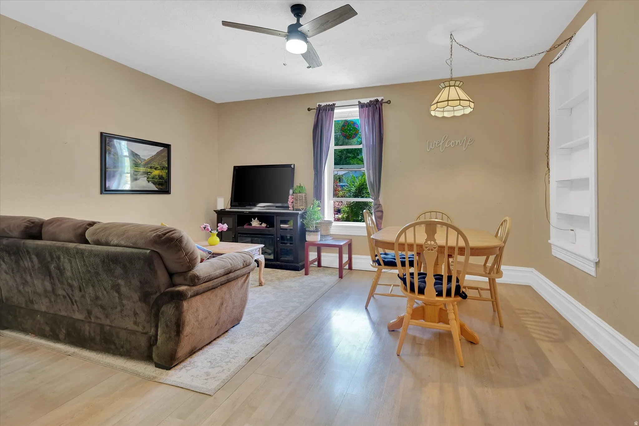 Open concept living space featuring hard flooring, a ceiling fan with integrated lighting, a built-in wall shelf unit, and a window with natural light