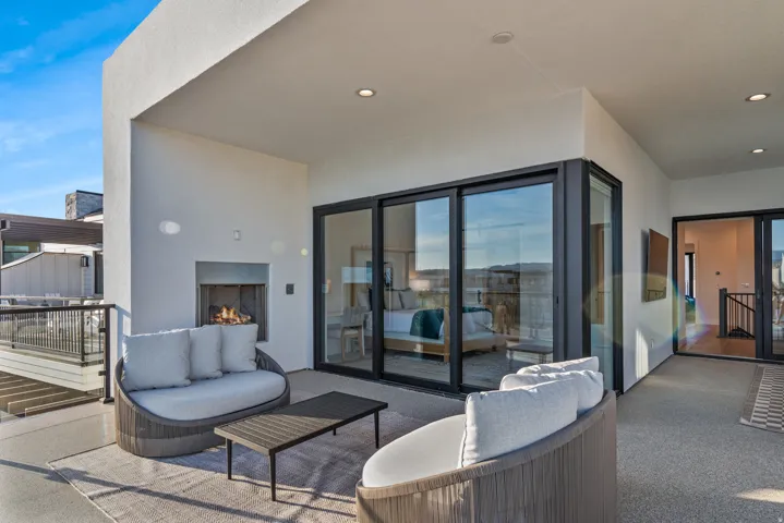 Spacious outdoor terrace with a built-in fireplace, modern black-framed sliding glass doors, and recessed lighting
