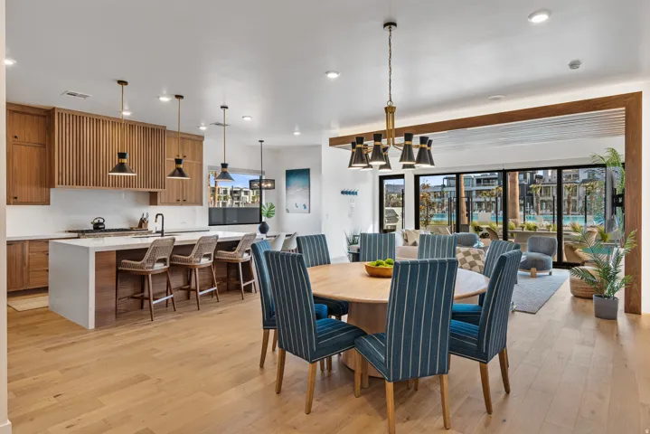 Open-concept living space with light wood-finish flooring, a kitchen featuring wood cabinetry and an island with seating, and a dining area illuminated by a modern chandelier