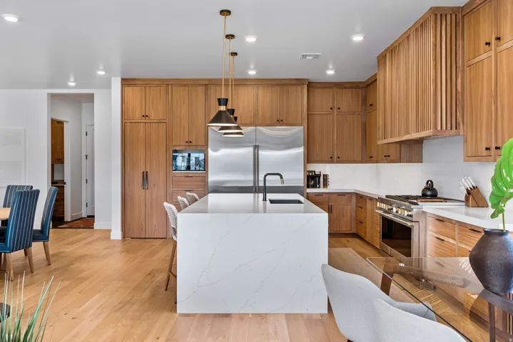 Gourmet kitchen featuring a waterfall island with a built-in sink, stainless steel appliances, wood-finish cabinetry, and recessed lighting