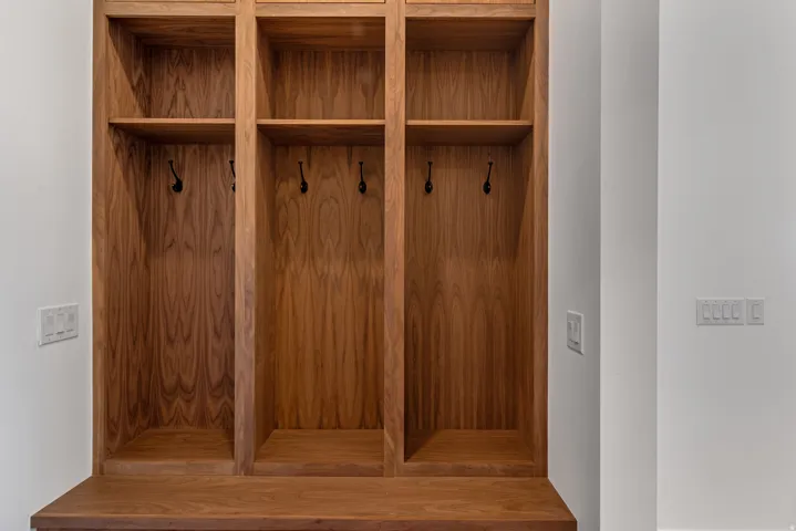 Custom wood-finish mudroom built-ins featuring three individual cubbies with upper shelving, lower storage compartments, and matte black coat hooks