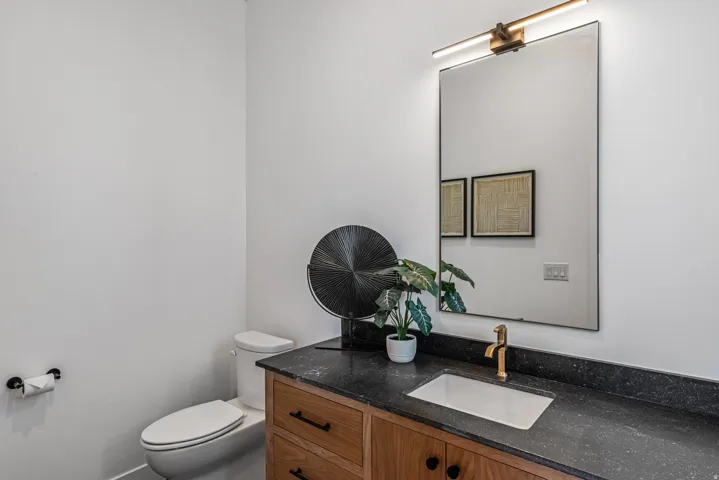 Bathroom vanity featuring a wood-finish cabinet, dark speckled countertop, and integrated rectangular sink with a gold-tone faucet