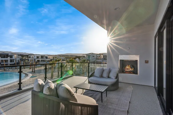 Spacious balcony featuring an outdoor fireplace, dark-framed sliding glass doors, a glass and metal railing, and textured concrete flooring