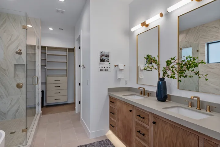 Spacious bathroom featuring a dual vanity with wood-finish cabinetry, integrated sinks, and gold-toned fixtures
