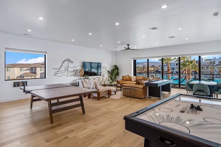 Expansive entertainment space featuring wood-finish flooring, recessed lighting, floor-to-ceiling windows, and a ceiling fan