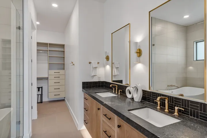 Bathroom featuring a double vanity with wood-finish cabinetry, dark stone countertops, and rectangular undermount sinks