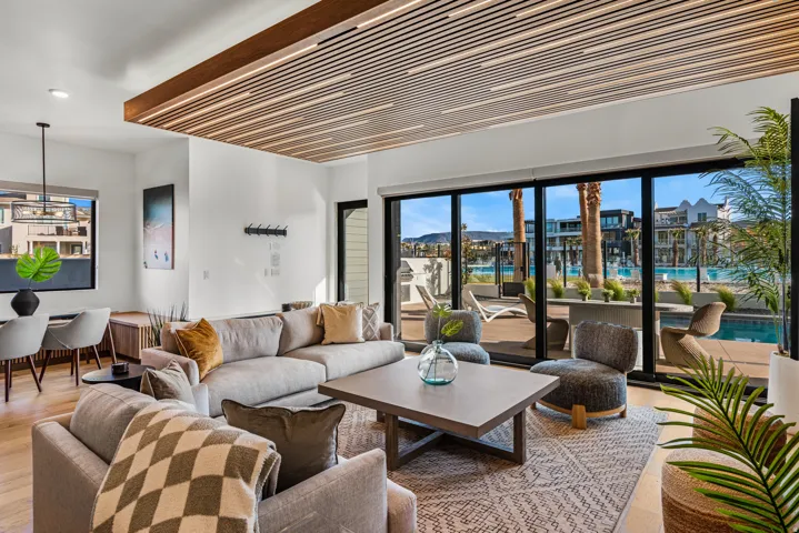 Open-concept living space featuring a wood-slat ceiling detail with integrated lighting, expansive floor-to-ceiling sliding glass doors, and light wood-finish flooring