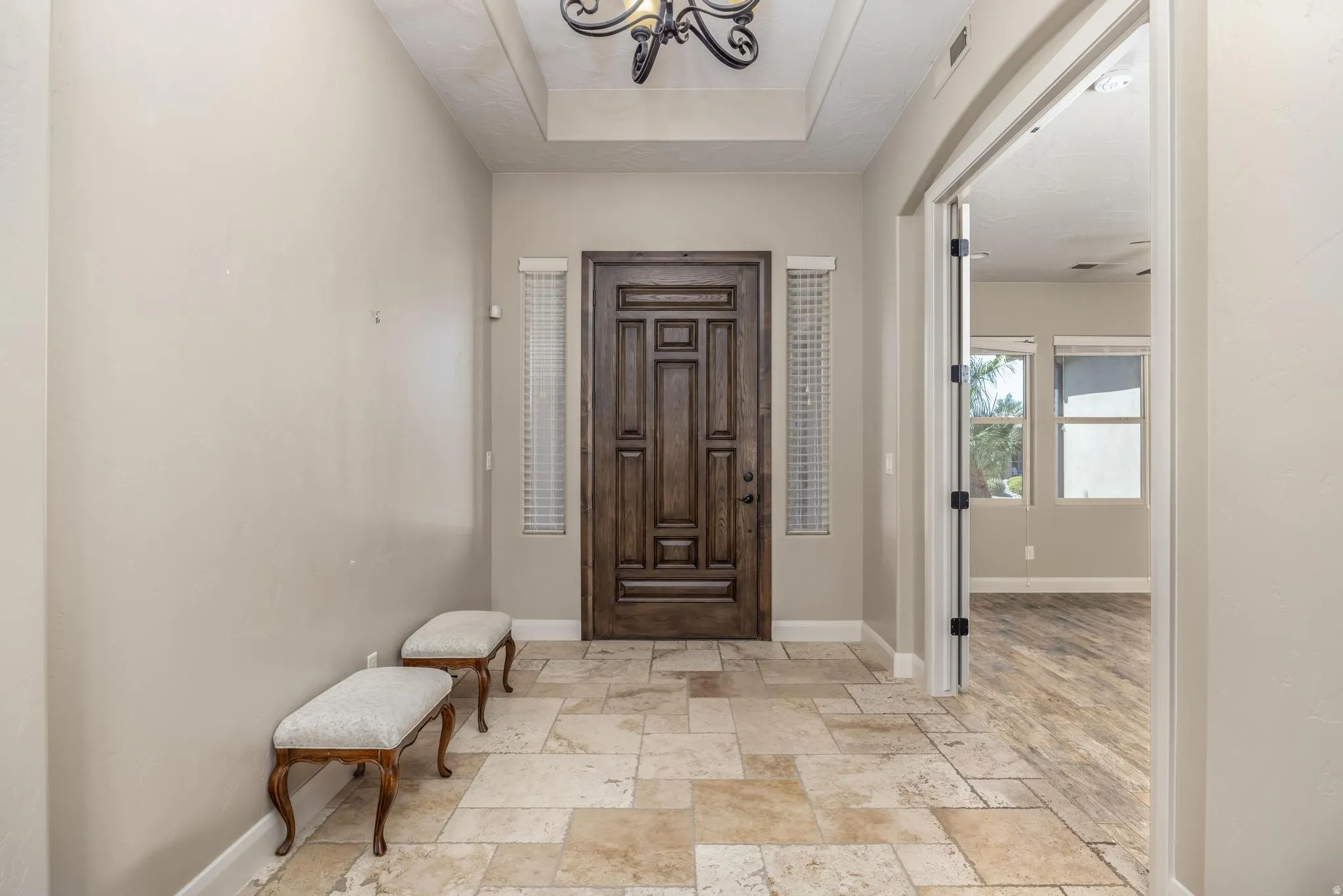 Entry foyer featuring a coffered ceiling with an ornate chandelier, a paneled wood-finish entry door, and stone tile flooring