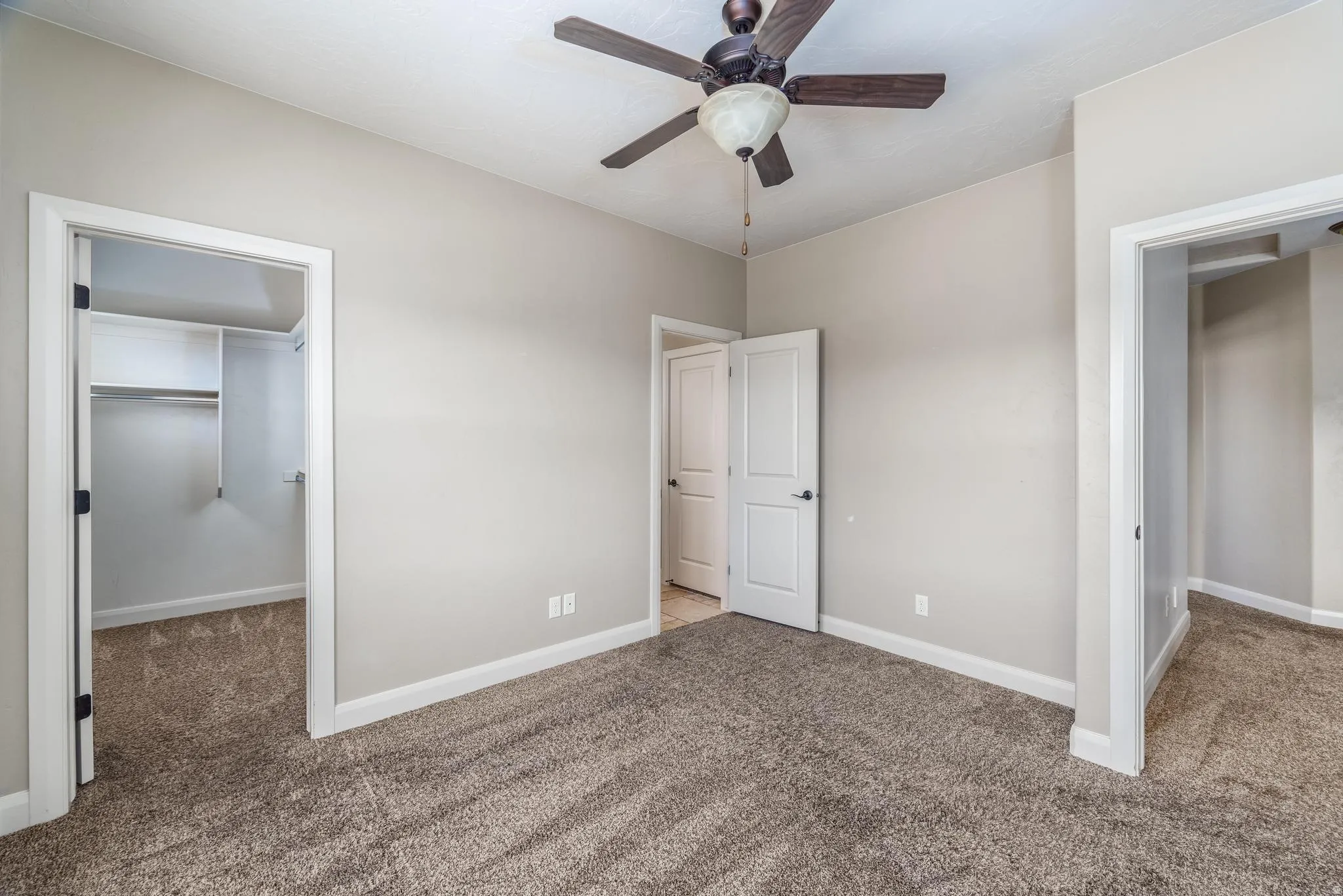 Carpeted room with a ceiling fan, light gray walls, white trim, and a walk-in closet with built-in shelving