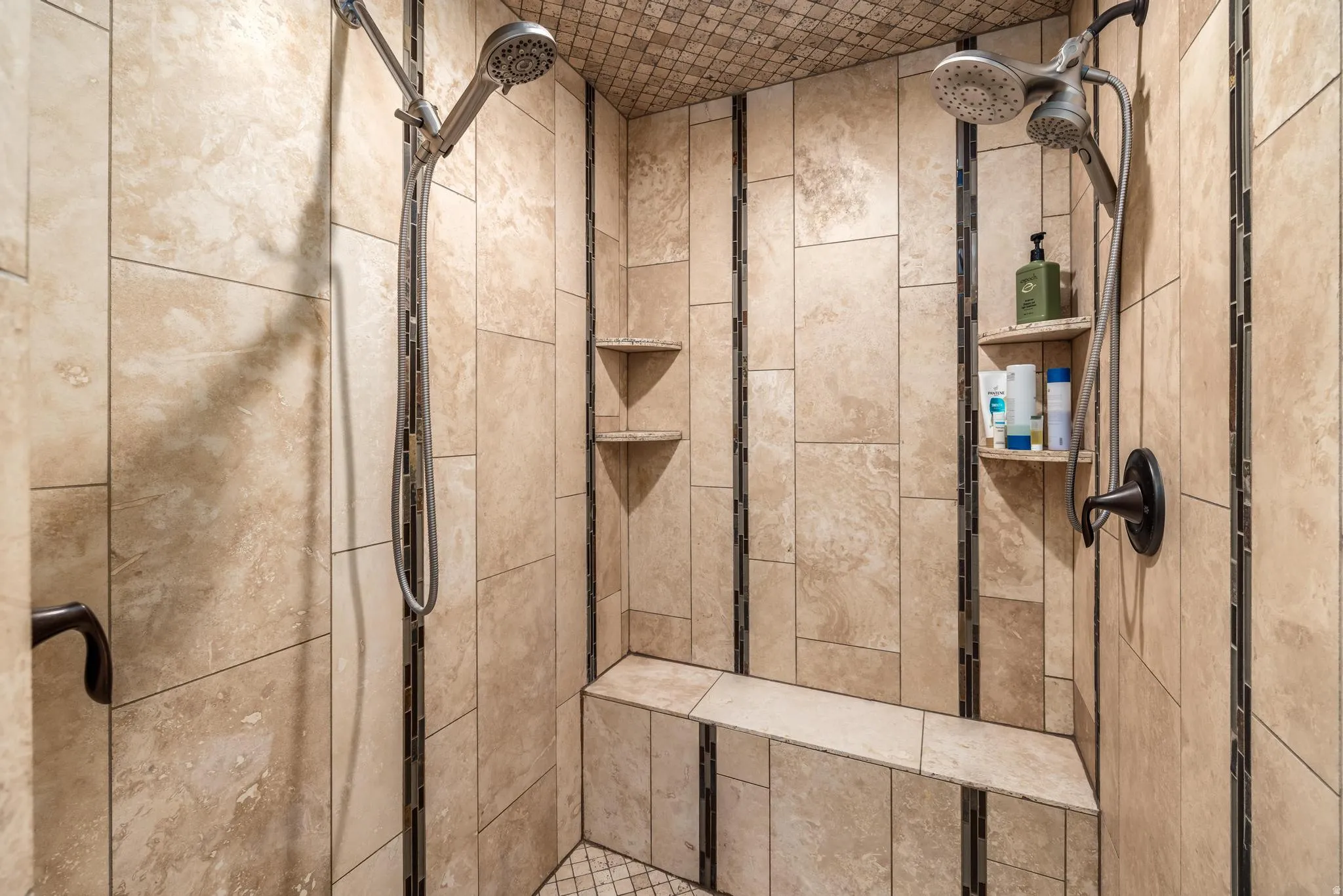 Tiled shower enclosure featuring a built-in bench, dual shower heads, and integrated corner shelving