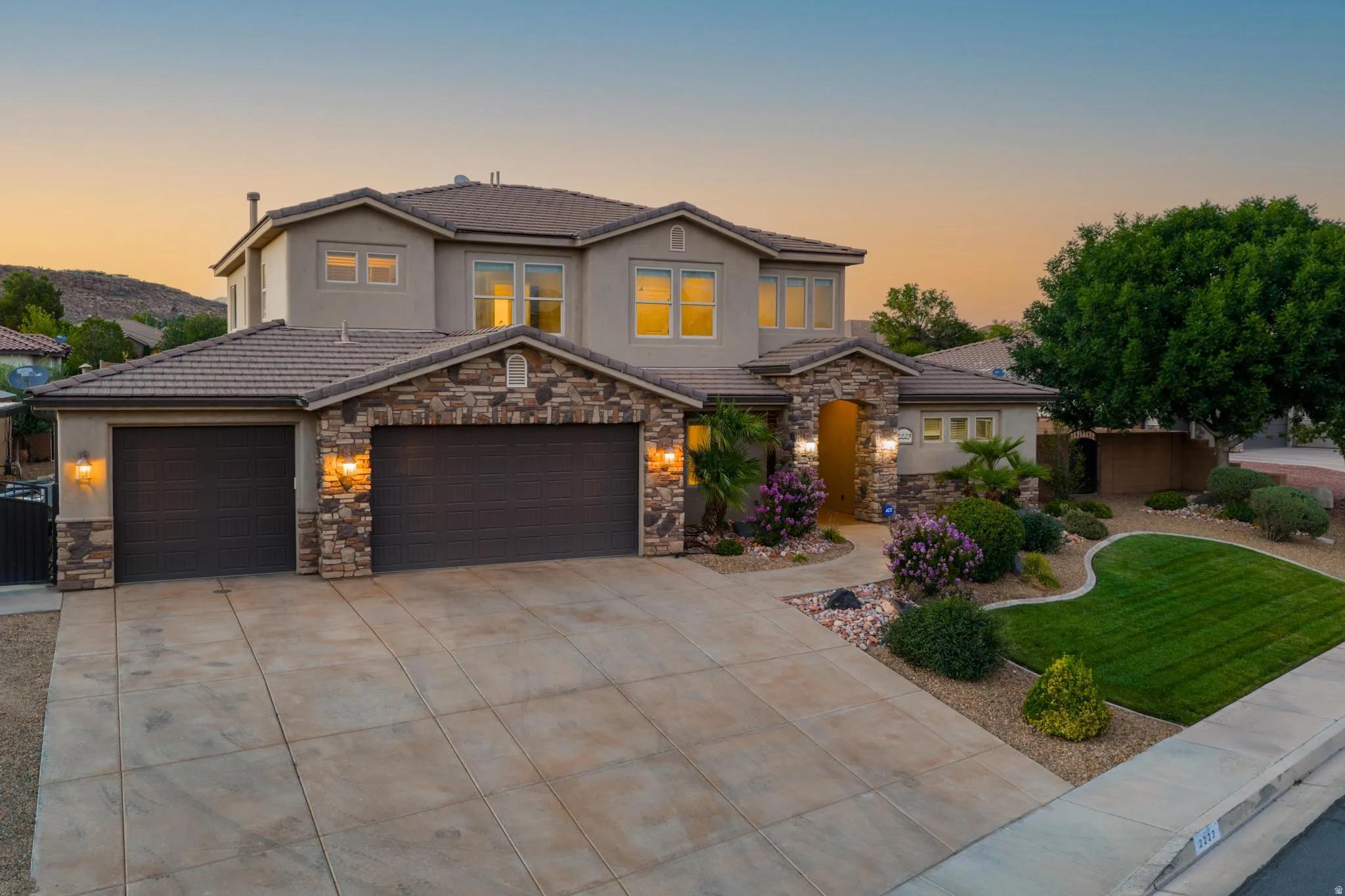 Stucco and stone facade property featuring a tile roof, multi-car garage, concrete driveway, and established landscaping