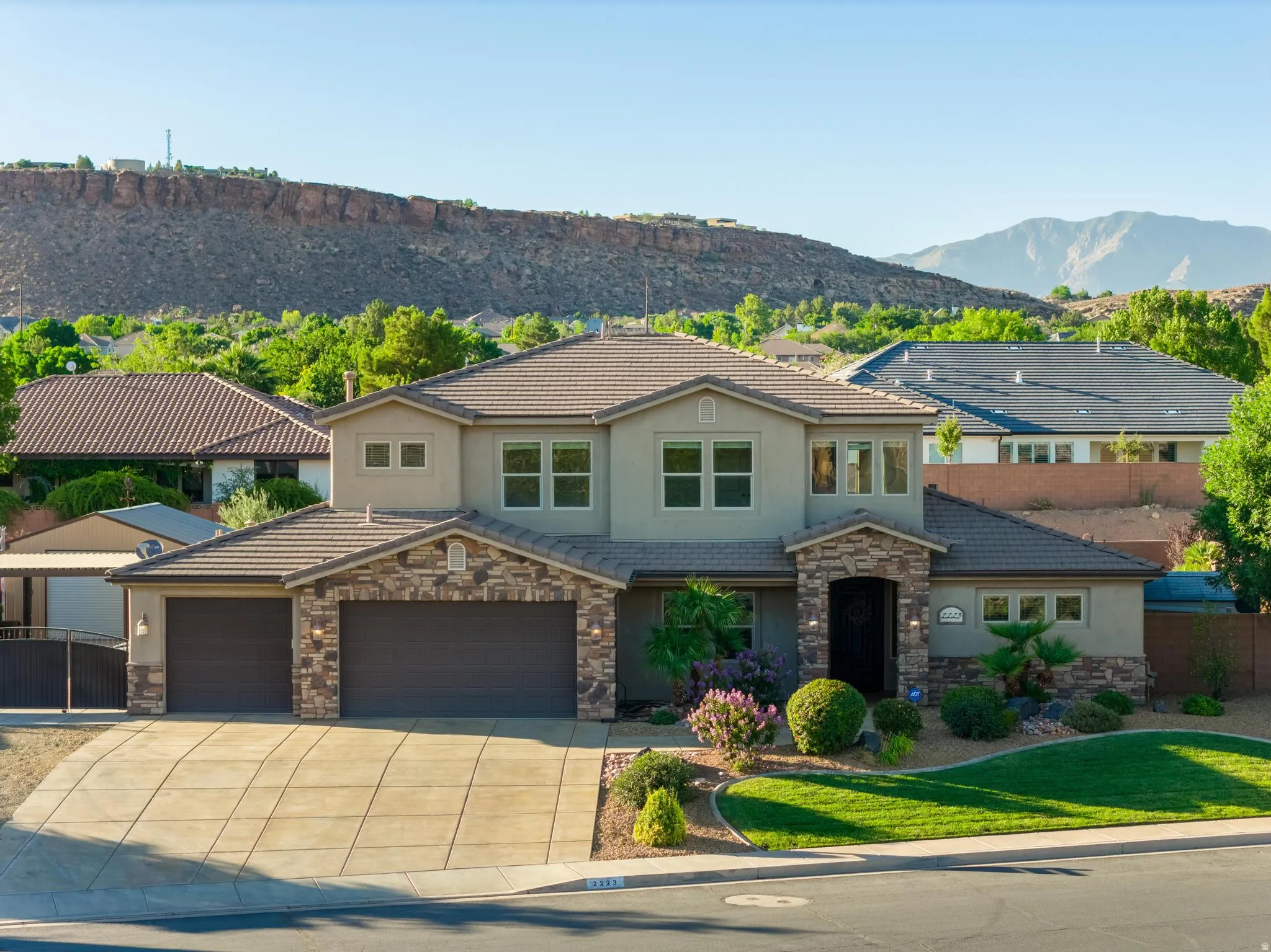 Two-story residence featuring a stone and stucco exterior, a tile roof, a multi-car garage, mature landscaping, and mountain scenery