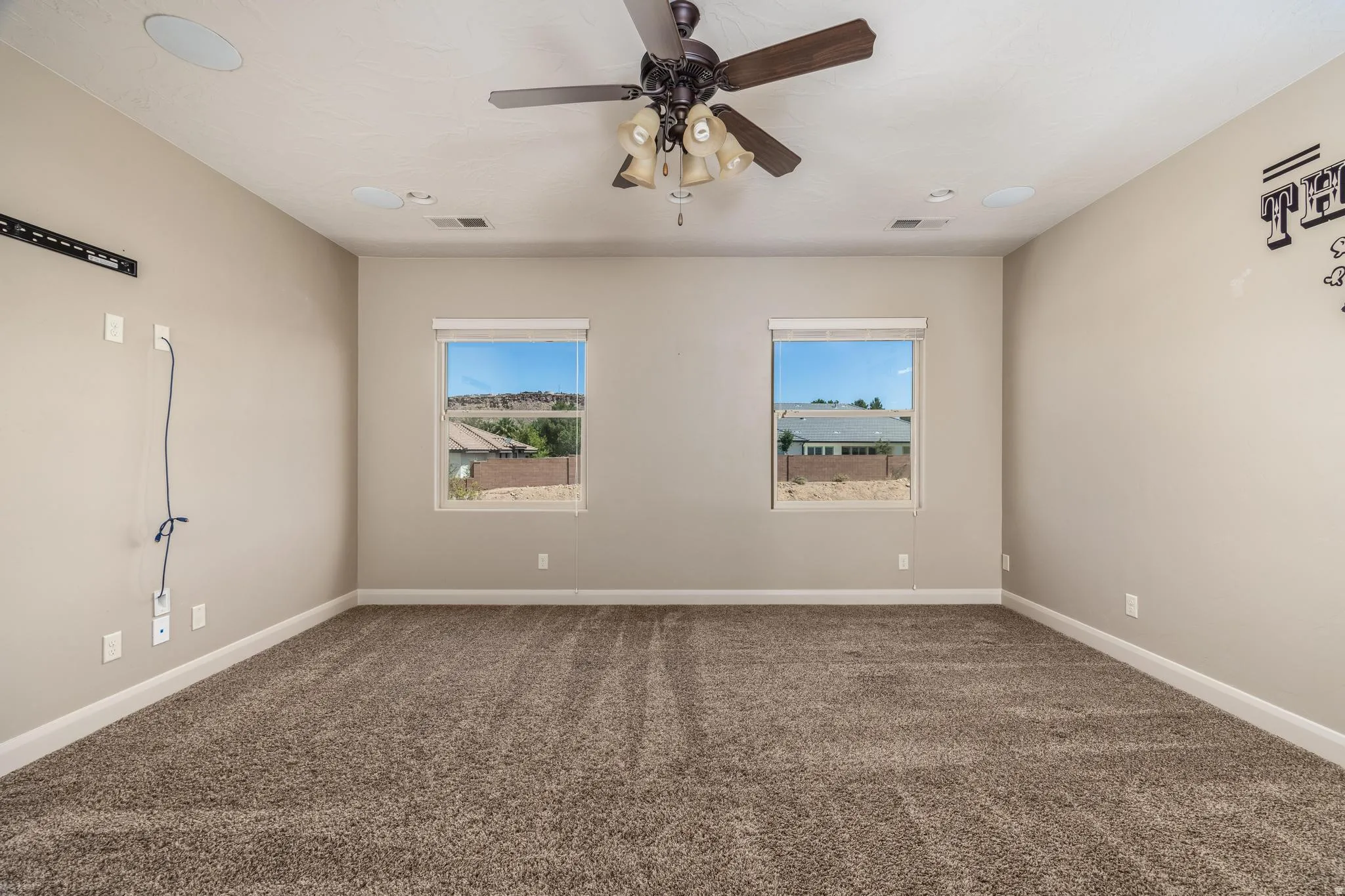 Carpeted room featuring two windows, a ceiling fan with integrated lighting, and recessed ceiling speakers