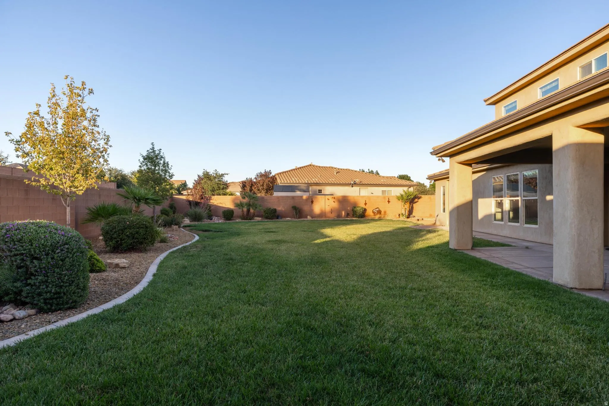 Expansive backyard featuring a lush lawn, mature landscaping, and a covered patio area