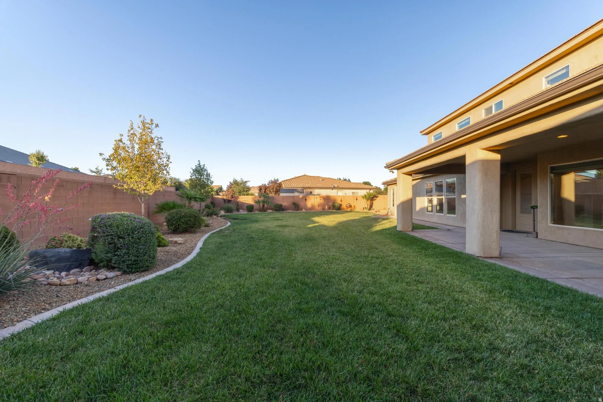 Expansive green lawn with a defined landscape border, mature shrubbery, and a covered patio area